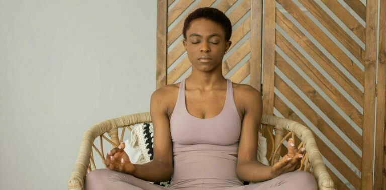 Woman meditating indoors in a comfortable chair, focusing on wellness and mindfulness.
