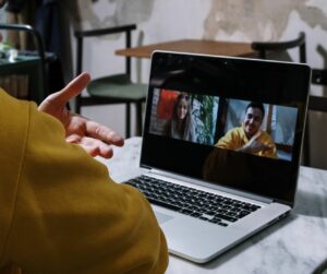 Person in a yellow sweater hosting a video call on a laptop indoors.