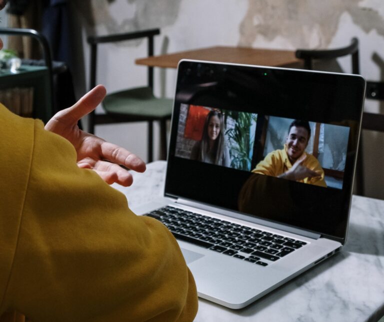 Person in a yellow sweater hosting a video call on a laptop indoors.